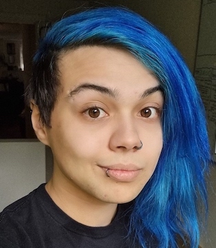 Portrait selfie of a 29 year old person with an undercut and medium legnth blue hair parted to the side. They are smiling and wearing a black shirt.
